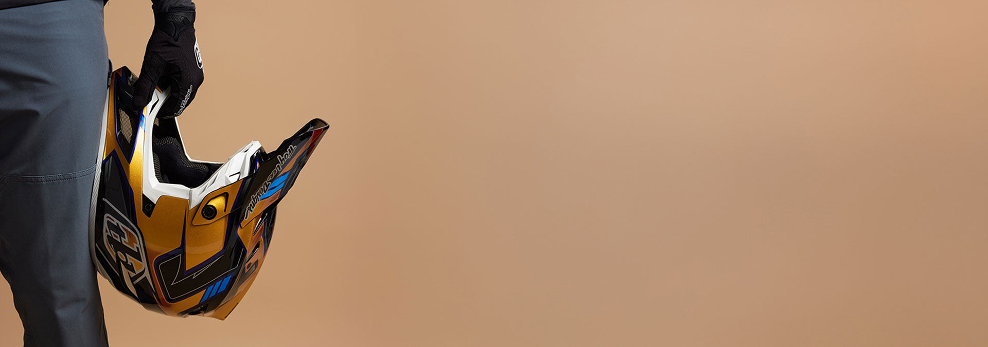 A rider holding a Troy Lee Designs full face helmet in front of a brown background